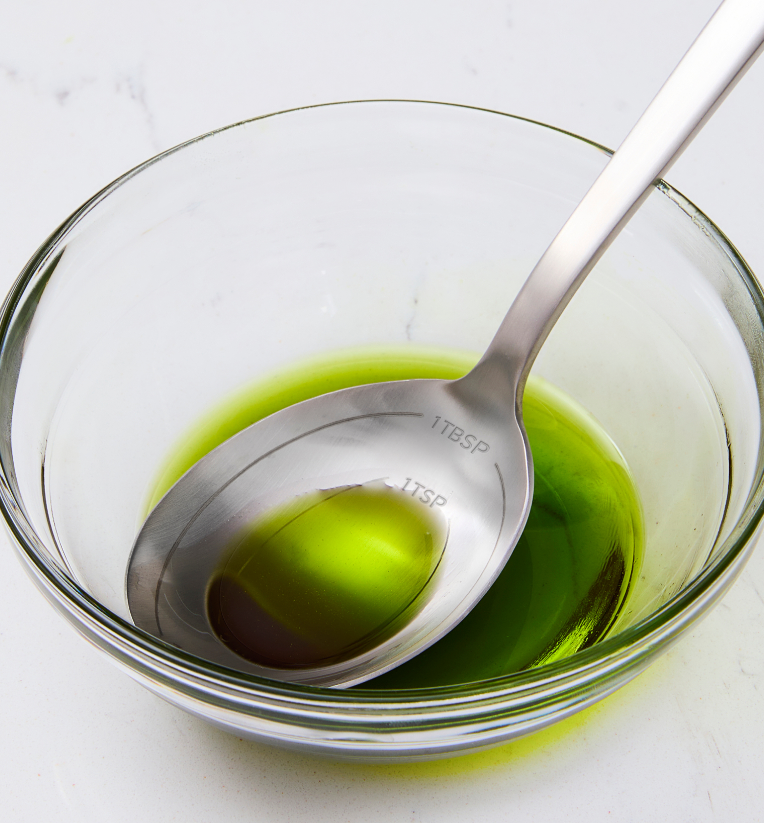 Bright green liquid in glass bowl with stainless steel measuring spoon showing 1 tablespoon and 1 teaspoon markings