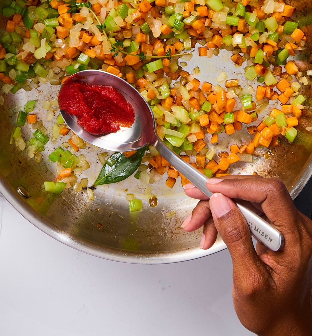 Adding tomato paste to sautéed mirepoix vegetables in a Misen stainless steel pan