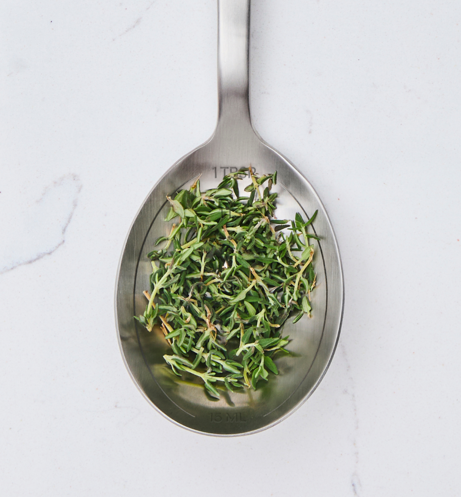 One tablespoon of fresh thyme leaves on stainless steel measuring spoon